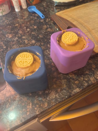 A navy and a purple FreezBox filled with a frozen treat and topped with a biscuit, on a kitchen counter