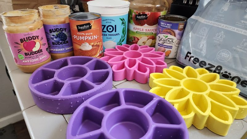 Purple and pink Freezbone toys on a counter next to pumpkin, yogurt and peanut butter